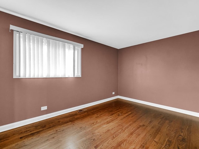 unfurnished room featuring baseboards, visible vents, and wood finished floors