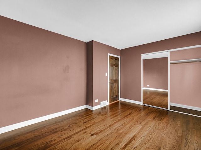 unfurnished bedroom with baseboards, visible vents, wood finished floors, and a closet