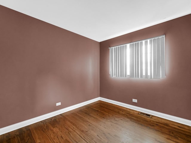 empty room featuring baseboards, dark wood-style flooring, and visible vents