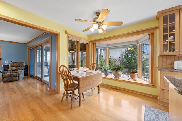 dining space featuring a ceiling fan, light wood-style flooring, crown molding, and baseboards