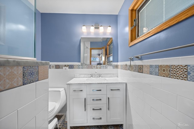 bathroom with vanity, toilet, a wainscoted wall, and tile walls