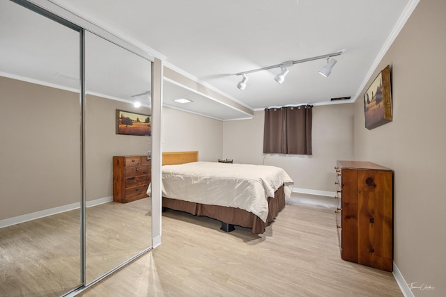 bedroom featuring light wood-style floors, baseboards, ornamental molding, and rail lighting