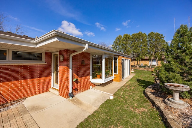 entrance to property with a lawn, a patio, and brick siding