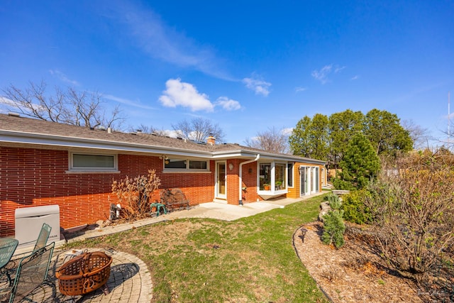 rear view of house with a fire pit, a patio, a chimney, a lawn, and brick siding