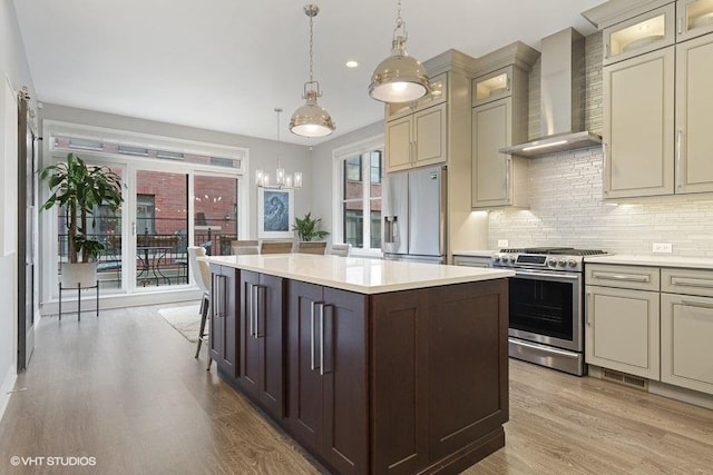 kitchen with wall chimney range hood, light countertops, light wood-style flooring, a center island, and stainless steel appliances