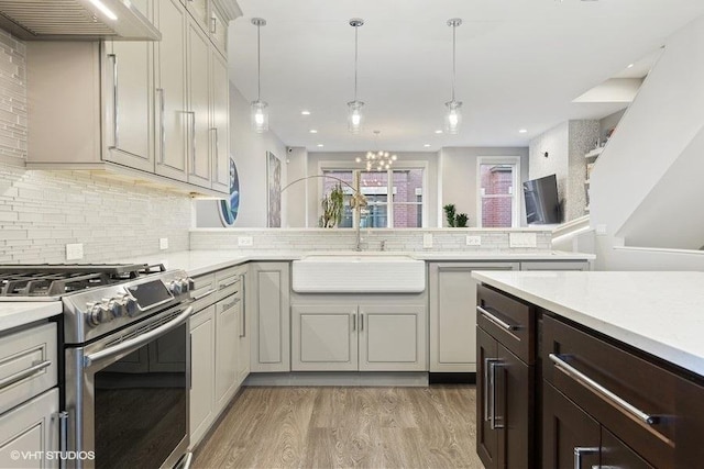 kitchen featuring decorative backsplash, stainless steel gas stove, light countertops, a sink, and light wood finished floors