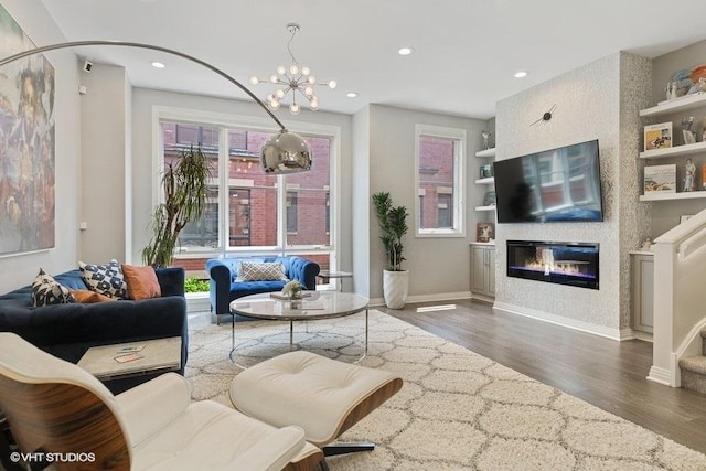 living room with an inviting chandelier, built in features, a glass covered fireplace, wood finished floors, and baseboards