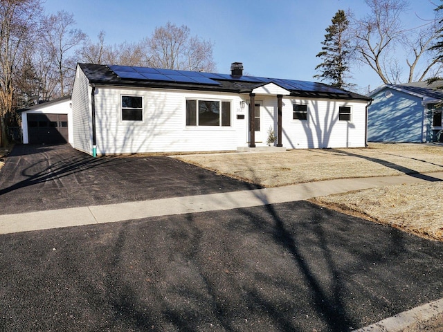 single story home featuring a chimney, a garage, solar panels, and an outbuilding