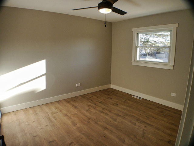 unfurnished room with wood finished floors, a ceiling fan, visible vents, and baseboards