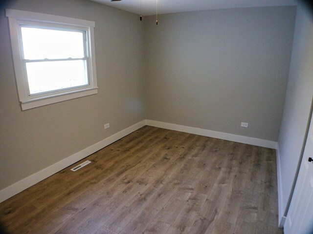 empty room with wood finished floors, visible vents, and baseboards