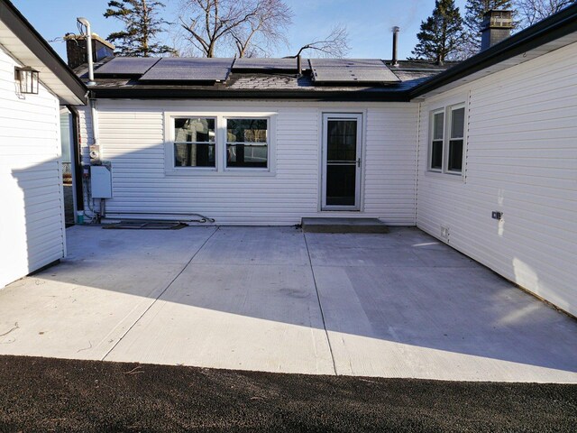rear view of house featuring a patio, solar panels, and a shingled roof