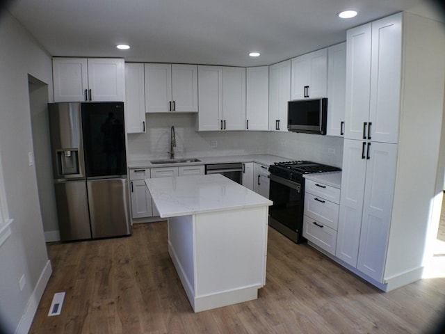 kitchen with appliances with stainless steel finishes, wood finished floors, white cabinets, and a sink