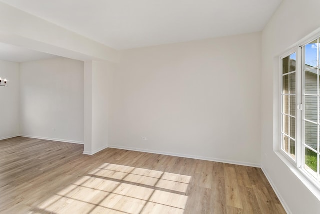 spare room featuring baseboards, a notable chandelier, and light wood-style floors