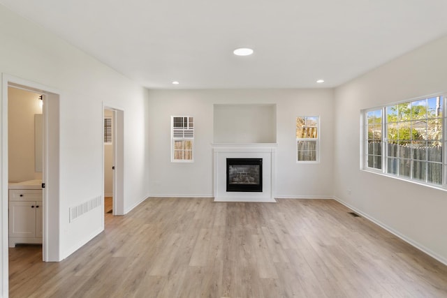 unfurnished living room with a glass covered fireplace, recessed lighting, baseboards, and light wood-type flooring