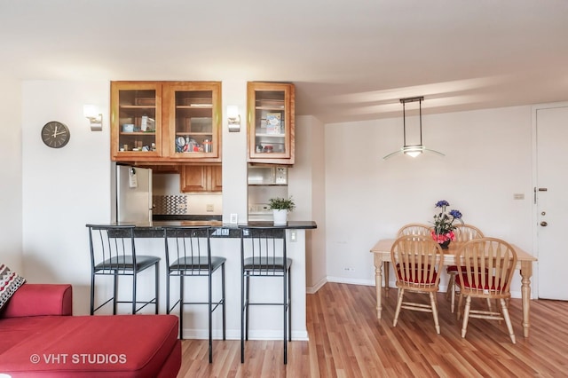 7061 N Kedzie Ave Unit 1409, Chicago, IL 60645 - kitchen featuring glass insert cabinets, freestanding refrigerator, light wood-style floors, brown cabinets, and a kitchen breakfast bar