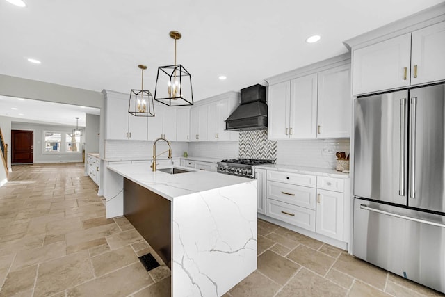 kitchen featuring recessed lighting, freestanding refrigerator, a sink, stone tile floors, and premium range hood