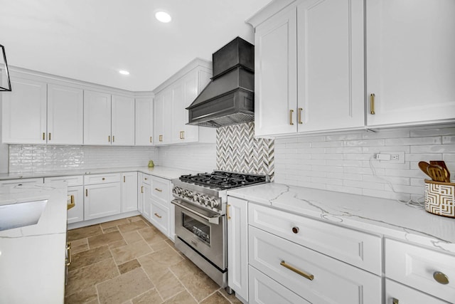 kitchen featuring light stone countertops, decorative backsplash, custom range hood, high end stove, and white cabinetry