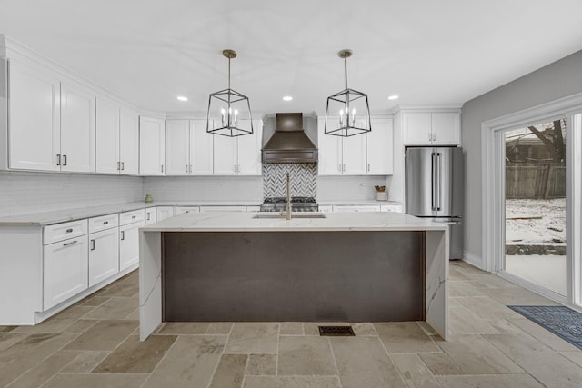 kitchen with stone tile floors, tasteful backsplash, premium range hood, freestanding refrigerator, and a notable chandelier