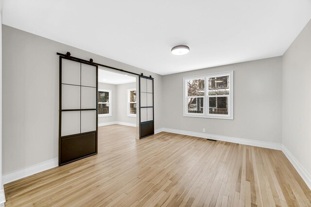 spare room with light wood-style floors, baseboards, visible vents, and a barn door