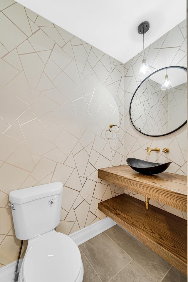 half bath with tile walls, tile patterned floors, toilet, and a sink