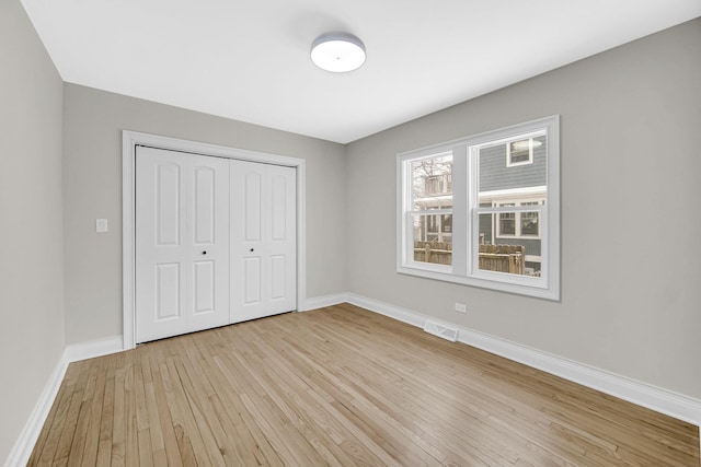 unfurnished bedroom featuring light wood-style floors, a closet, visible vents, and baseboards