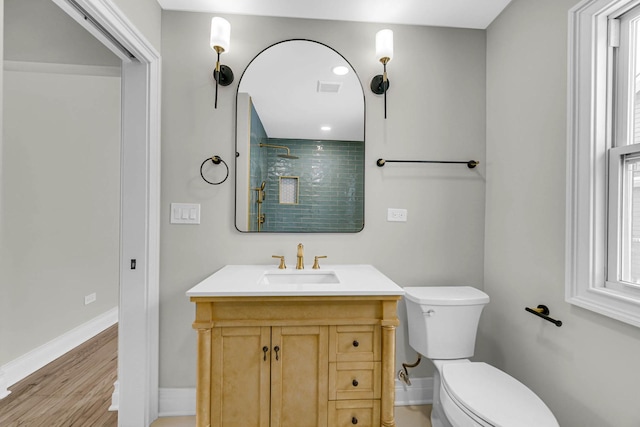 bathroom featuring a tile shower, toilet, vanity, baseboards, and visible vents