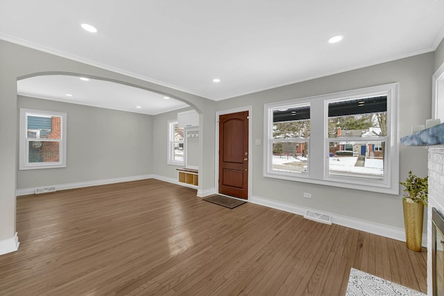 unfurnished living room featuring wood finished floors, visible vents, and arched walkways