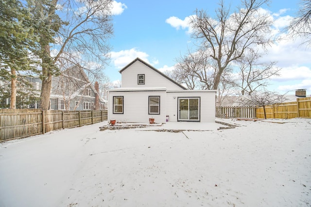 snow covered back of property featuring a fenced backyard