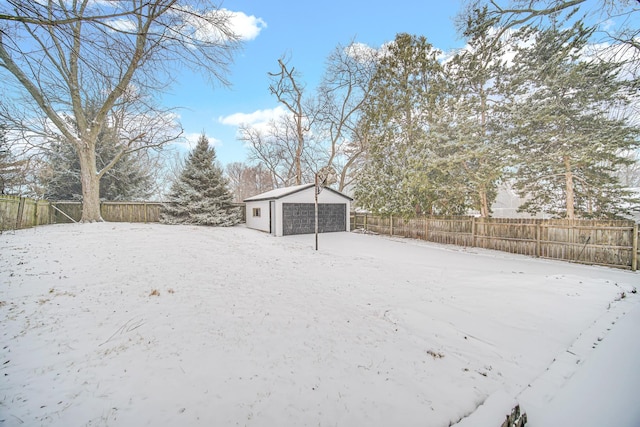 snowy yard featuring an outdoor structure, a garage, and a fenced backyard