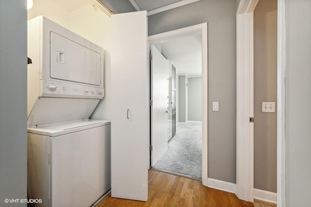 clothes washing area featuring light wood-type flooring, baseboards, laundry area, and stacked washer and dryer
