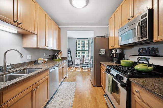 kitchen with dark stone countertops, appliances with stainless steel finishes, a sink, and light wood-style floors