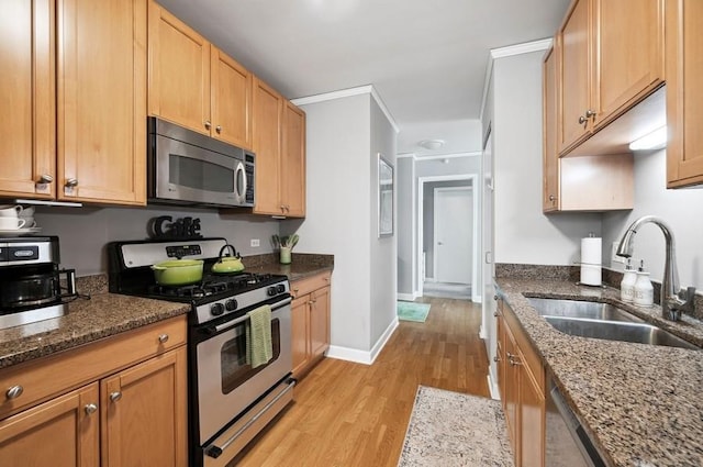kitchen featuring a sink, baseboards, light wood finished floors, dark stone counters, and stainless steel appliances