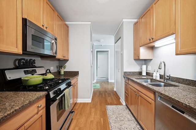kitchen featuring appliances with stainless steel finishes, a sink, light wood-style flooring, dark stone counters, and baseboards