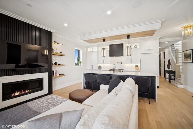 living area featuring crown molding, light wood-style floors, baseboards, recessed lighting, and stairs