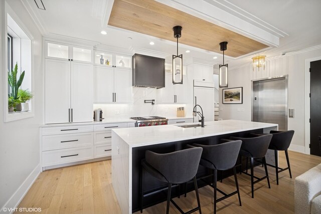 kitchen with a breakfast bar area, a sink, baseboards, wall chimney exhaust hood, and a kitchen island with sink
