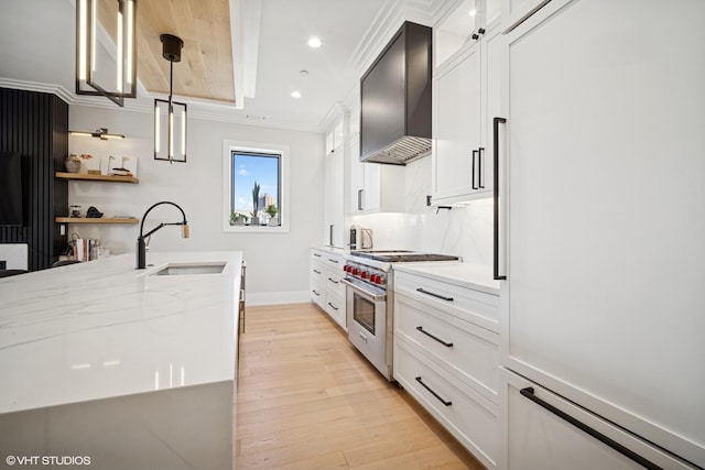 kitchen with wall chimney range hood, a sink, light wood-type flooring, premium appliances, and crown molding