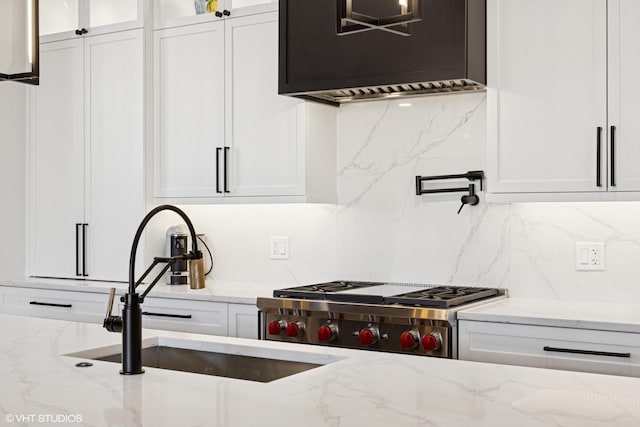 kitchen with a sink, glass insert cabinets, light stone counters, backsplash, and white cabinets