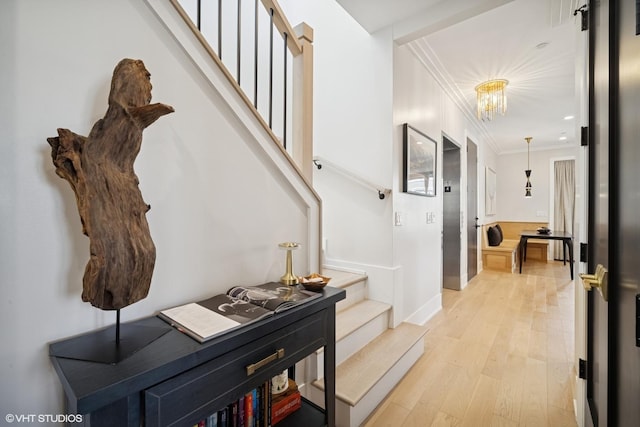 hall featuring crown molding, baseboards, an inviting chandelier, light wood-type flooring, and stairs