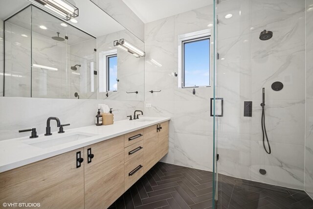 full bath with double vanity, tile walls, a marble finish shower, and a sink