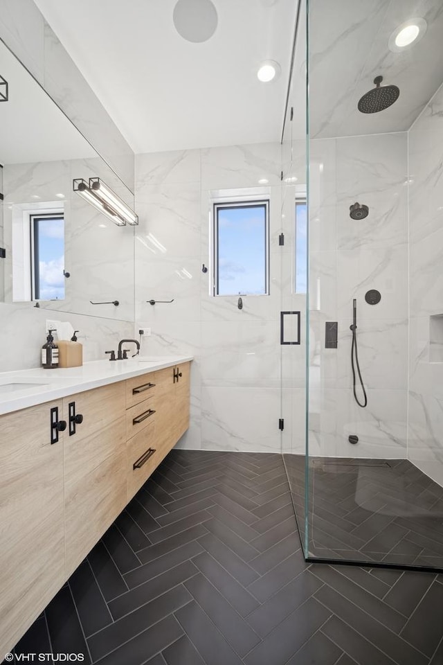 full bathroom featuring double vanity, tile walls, plenty of natural light, and a marble finish shower