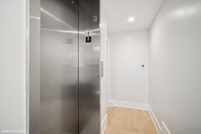 hallway with baseboards, recessed lighting, elevator, and light wood-style flooring