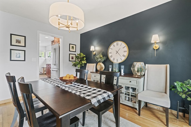 dining area featuring light wood-style floors, an accent wall, baseboards, and a chandelier