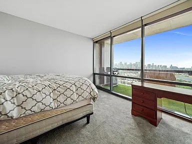 bedroom with carpet flooring, a wall of windows, and a view of city