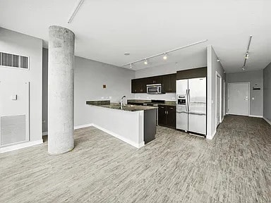 kitchen with decorative columns, rail lighting, appliances with stainless steel finishes, open floor plan, and light wood-style floors
