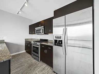 kitchen with stainless steel appliances, light stone counters, light wood-type flooring, track lighting, and baseboards