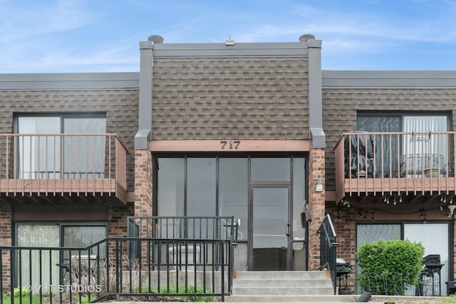 exterior space with brick siding, roof with shingles, and a balcony