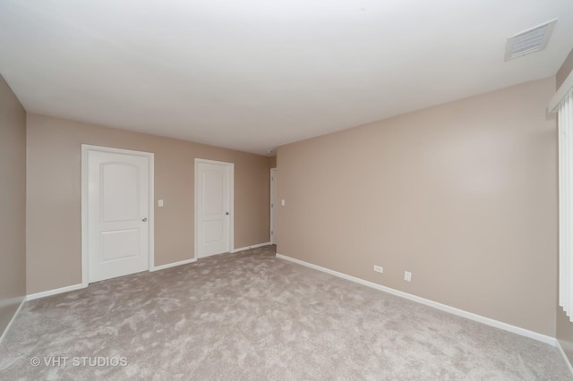 spare room featuring baseboards, light colored carpet, and visible vents