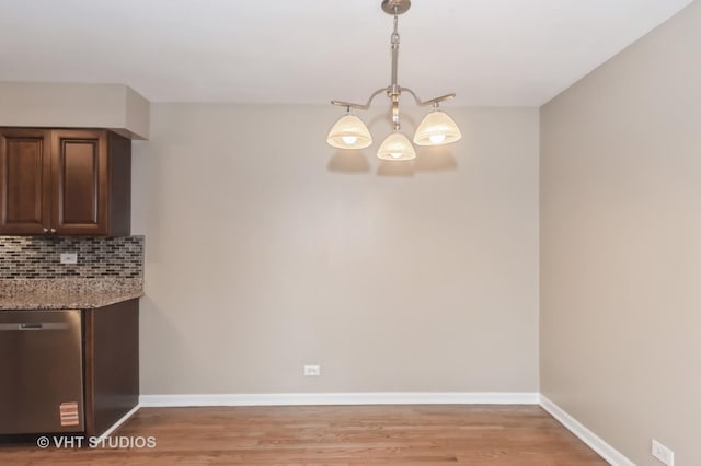 unfurnished dining area featuring baseboards, light wood-style flooring, and a notable chandelier