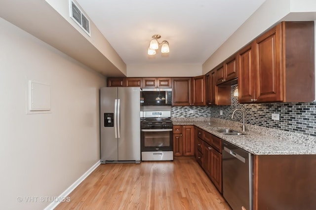 kitchen with appliances with stainless steel finishes, light stone counters, a sink, light wood finished floors, and visible vents
