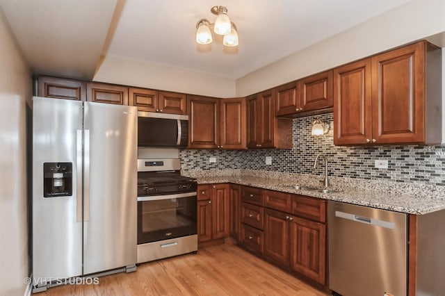 kitchen featuring backsplash, light stone countertops, a sink, light wood-style floors, and stainless steel appliances
